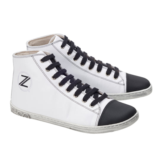 Die CHUQQS White von ZAQQ sind High-Top-Barfußschuhe mit einem weißen Nappaleder-Körper, ergänzt durch schwarze Schnürsenkel und Zehenkappen. Diese weißen Sneaker sind mit einem runden Logo mit dem Buchstaben „Z“ an der Seite versehen und haben leicht abgenutzt wirkende Sohlen für einen Hauch von Vintage-Flair.