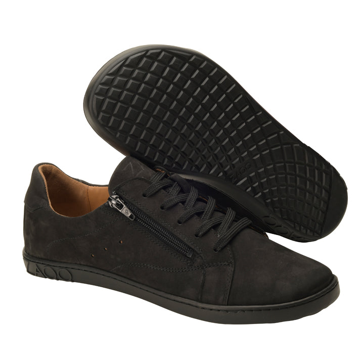 Die QOMFY Wide Black Sneaker von ZAQQ sind ein stylisches Paar mit schwarzen Schnürsenkeln und praktischen seitlichen Reißverschlüssen, abgerundet durch die markante ZAQQ SNEAKER-Sohle. Das Design hebt einen Schuh aufrecht und den anderen auf der Seite liegend hervor, um die gitterförmige Sohle zu präsentieren. Sie sind aus einem glatten, matten Material gefertigt und verfügen außerdem über ein hellbraunes Innenfutter.