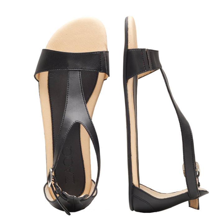 Entdecken Sie die ZAQQ CLIQ Vegan Black Sandalen aus atmungsaktiven veganen Materialien. Diese schwarzen Sandalen mit offener Spitze haben eine flache Sohle, einen breiten Riemen über dem Fuß und einen vertikalen Riemen, der mit einer Knöchelschnalle verbunden ist. Eine Sandale ist von oben abgebildet, während die andere von der Seite gezeigt wird.