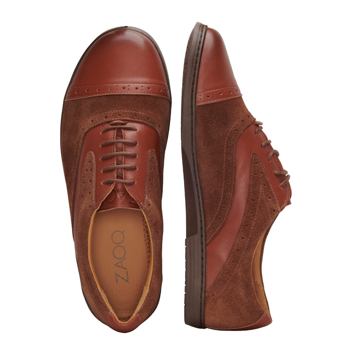 Ein Paar QENTLE Cognac Oxford-Schuhe von ZAQQ aus braunem Leder und Wildleder mit dekorativen Perforationen. Ein Schuh ist von oben zu sehen, der andere von der Seite, wodurch das Schnürdesign und die glatten Sohlen zur Geltung kommen.