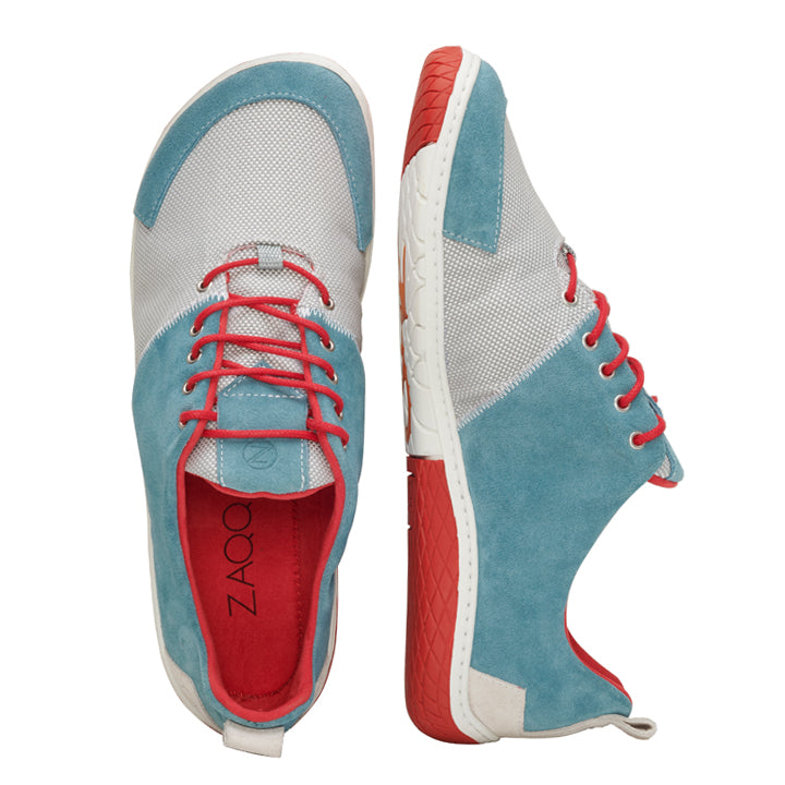 Wir präsentieren den QADIZ Blue von ZAQQ, ein Paar stylische Sneaker mit Akzenten aus blauem Wildleder, roten Schnürsenkeln und leuchtend roten Sohlen. Diese Barfußschuhe kombinieren atmungsaktives Mesh mit glattem Leder in Grau- und Blautönen für optimalen Komfort und Stil.