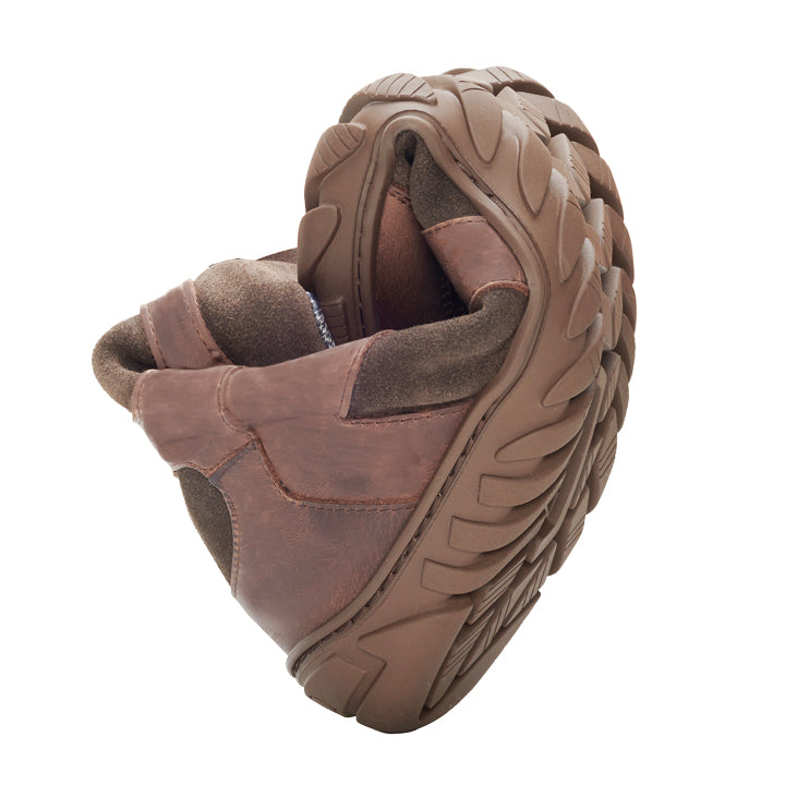 Der EXPLORER Brown Waterproof von ZAQQ ist ein Lederschuh mit einer dicken, robusten Sohle, die in der Mitte gebogen ist, um seine Flexibilität zu demonstrieren. Dieser Schuh ist auf Komfort und Haltbarkeit ausgelegt und außerdem wasserdicht, ideal für jedes Abenteuer.