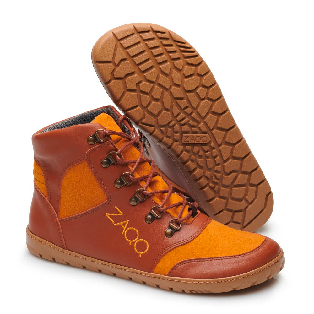 Ein Paar orange-braune High-Top-Sneaker mit schwarzen Schnürsenkeln wird durch eine strukturierte hellbraune Sohle hervorgehoben. Diese HIQE Vegan Sierra Waterproof-Schuhe von ZAQQ sind so konzipiert, dass sie den Elementen standhalten. Einer steht aufrecht und der andere liegt auf der Seite, um das einzigartige Sohlendesign zu präsentieren.