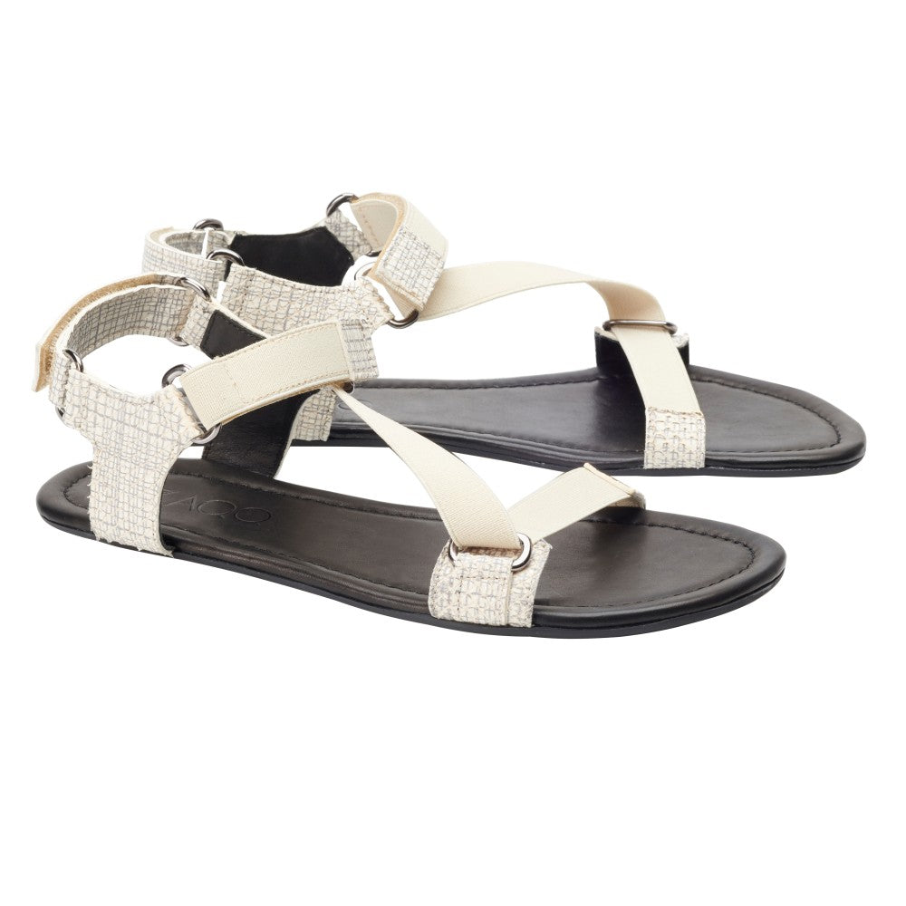 Wir präsentieren die MIQA Beige von ZAQQ: ein stilvolles Paar beige-schwarzer Sandalen mit gekreuzten Riemen und einer Schnalle auf der Rückseite, gefertigt aus hochwertigem Veloursleder. Mit einer flexiblen Sohle für ultimativen Komfort verbinden diese Barfußsandalen Stil mit Funktionalität und werden elegant vor einem weißen Hintergrund präsentiert.