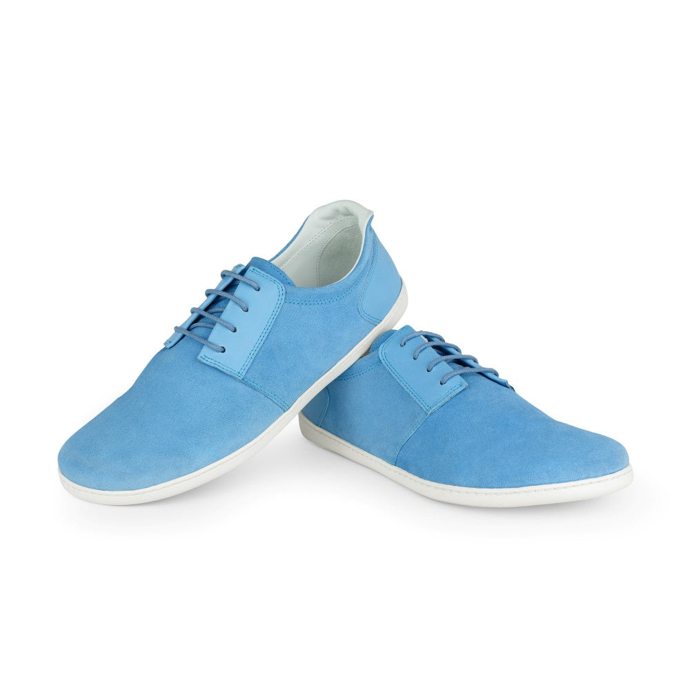 Ein Paar PIQUANT Azure Sneaker von ZAQQ mit samtig-blauem Finish, weißer Sohle und passenden blauen Schnürsenkeln. Ein Schuh lehnt kunstvoll an dem anderen vor einem schlichten weißen Hintergrund.