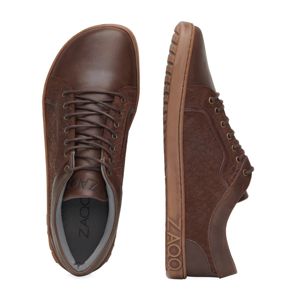 Der QODY Brown von ZAQQ ist ein Paar braune Lederschuhe aus hochwertigem Nappa- und Veloursleder. Das Design zeigt einen Schuh von oben und den anderen von der Seite, wobei das strukturierte Muster, die braunen Schnürsenkel und die flexible Barfußsohle hervorgehoben werden. „ZAQQ“ ist stilvoll auf der Sohle des Schuhs in der Seitenansicht eingraviert.