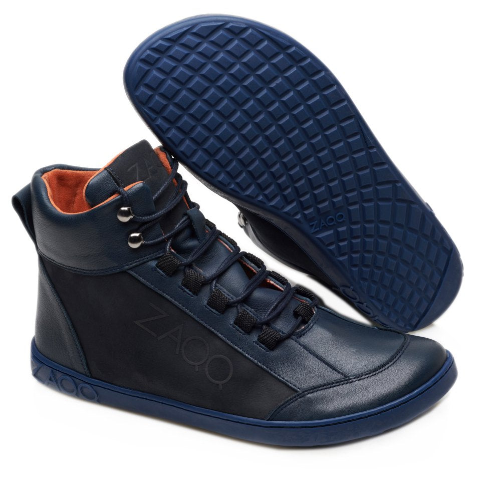 Wir präsentieren den WALQER Navy von ZAQQ: Dieser High-Top-Sneaker hat eine stylische marineblaue Außenseite mit einem auffälligen roten Innenfutter und einer flexiblen blauen Gummisohle. Der Schuh ist mit schwarzen Schnürsenkeln versehen und zeigt stolz das ZAQQ-Logo an der Seite. Ein Sneaker steht aufrecht, während sein Gegenstück angewinkelt ist, um das komplizierte Sohlenmuster zu präsentieren, das den typischen Komfort und Stil von Barfußboot widerspiegelt.