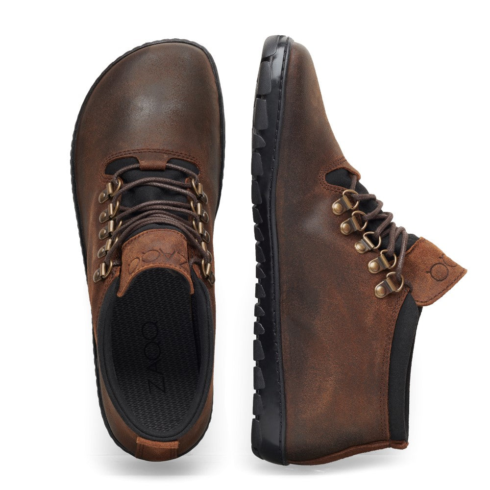 Ein Paar EXPEQ Mid Brown Waterproof-Schuhe von ZAQQ, gefertigt aus braunem Leder mit schwarzen Sohlen und ausgestattet mit sechs Metallösen zum Schnüren. Sie verfügen über ein rundes Zehendesign und eine gepolsterte schwarze Innensohle, wobei ein Schuh von oben und der andere von der Seite gezeigt wird.